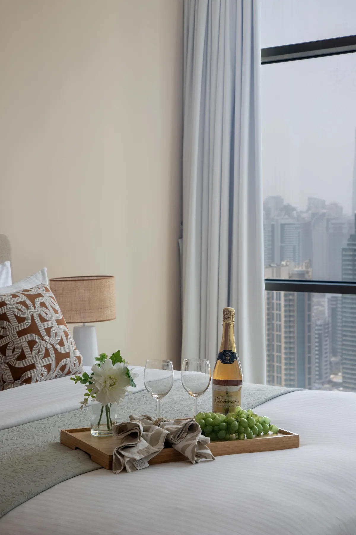 Un dormitorio con una cama junto a una gran ventana con edificios de la ciudad a la vista.