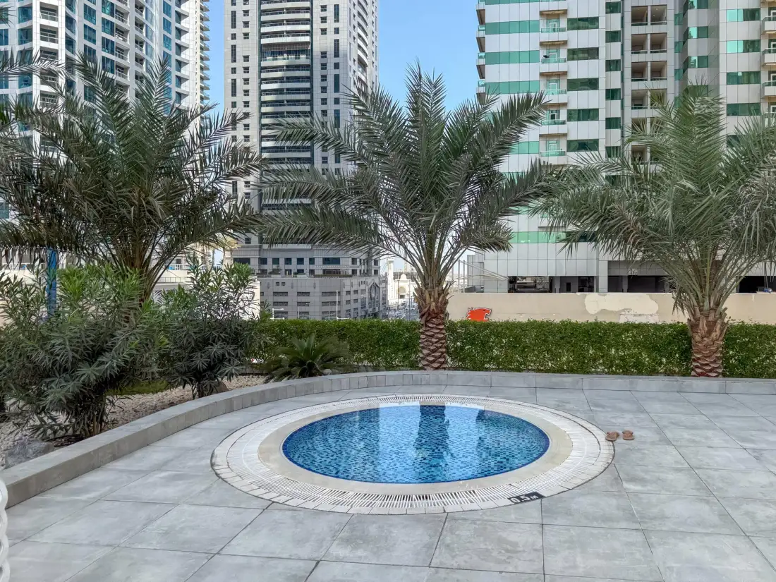 Una piscina al aire libre está rodeada de palmeras y edificios altos.