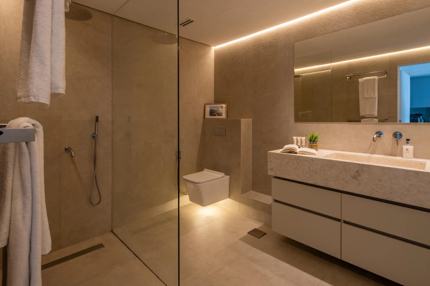 Un baño moderno con una ducha de vidrio y un amplio lavabo bajo un espejo.