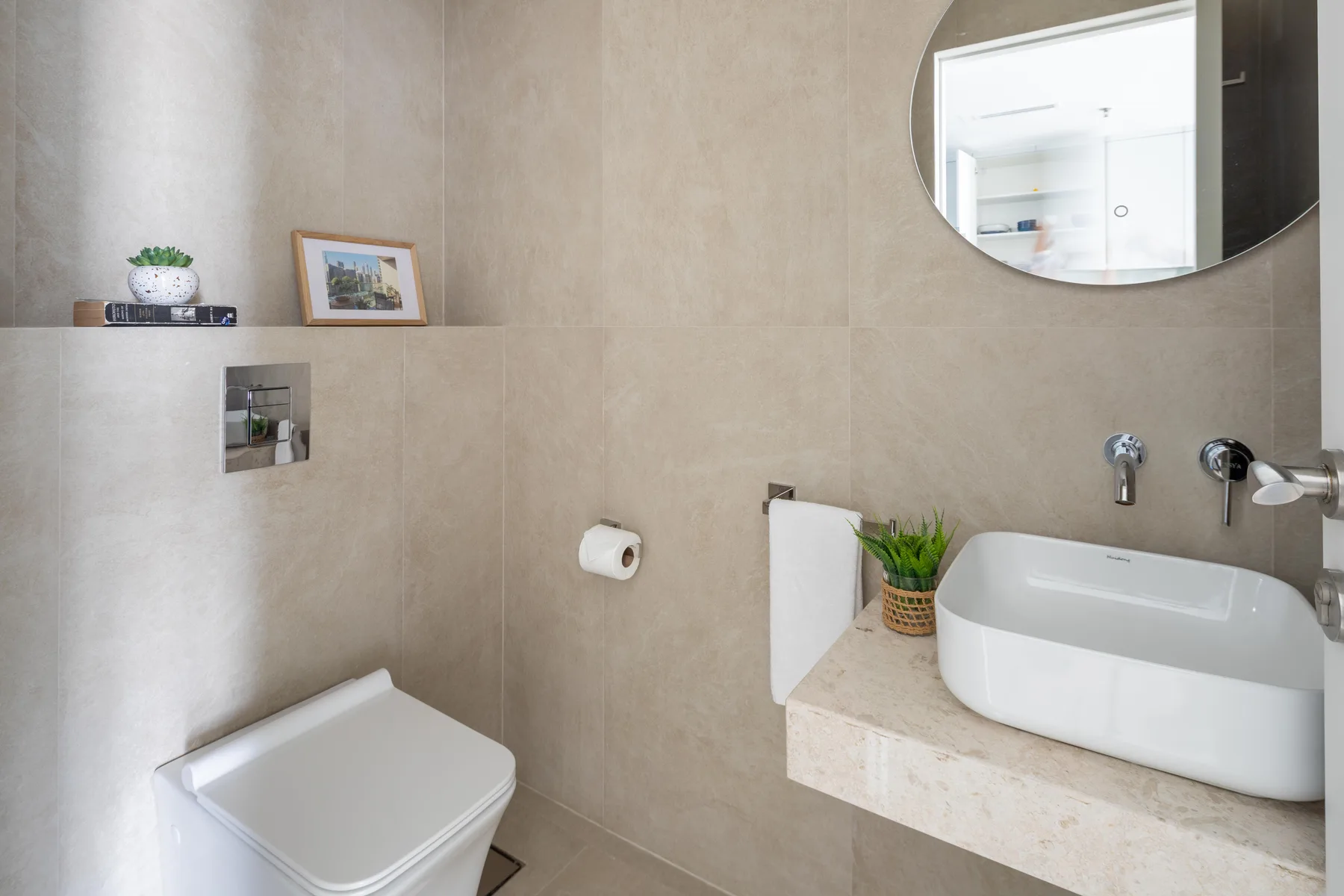 Un baño con un lavabo sobre la encimera y un inodoro bajo un espejo redondo.