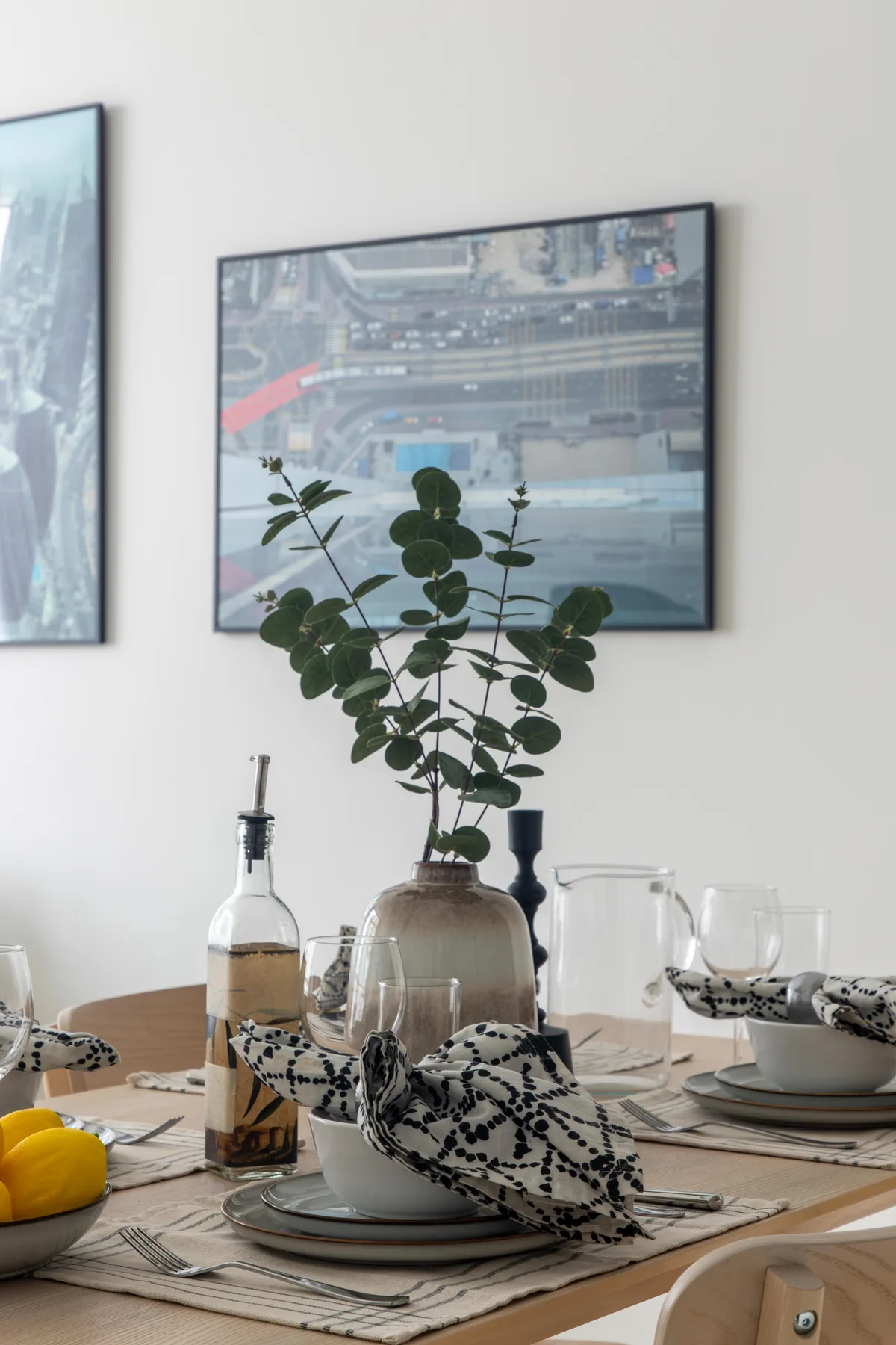 Una mesa de comedor está puesta con platos, vasos, servilletas estampadas y una planta frondosa.