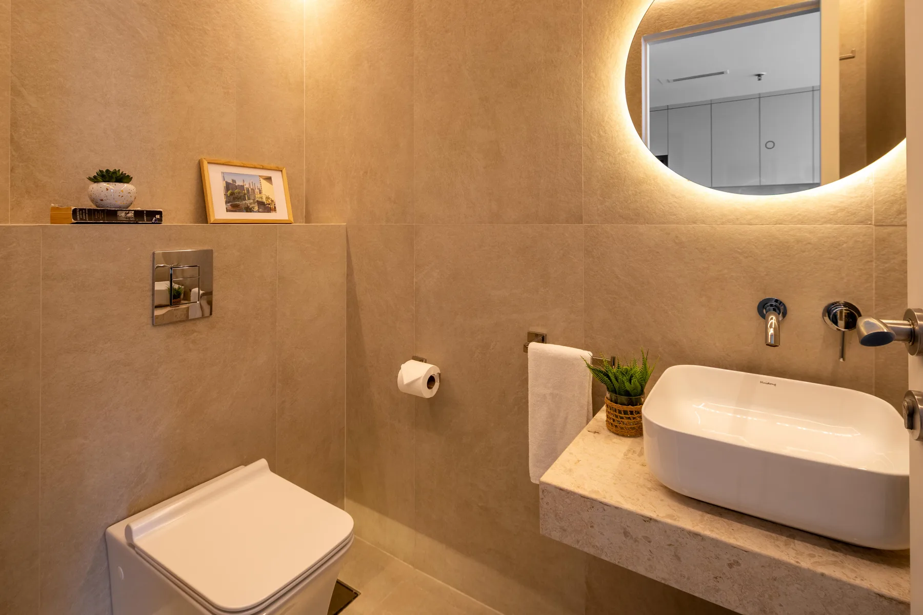 Un baño moderno con inodoro, lavabo y espejo redondo iluminado.
