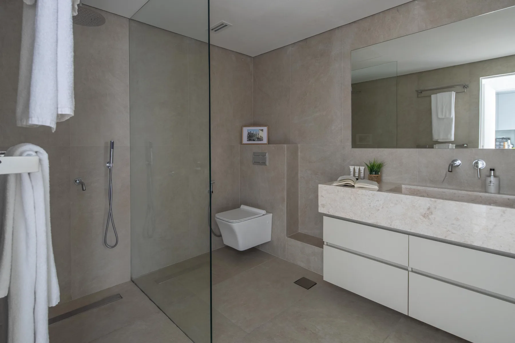 Un baño moderno con ducha de vidrio, inodoro suspendido y un amplio tocador.