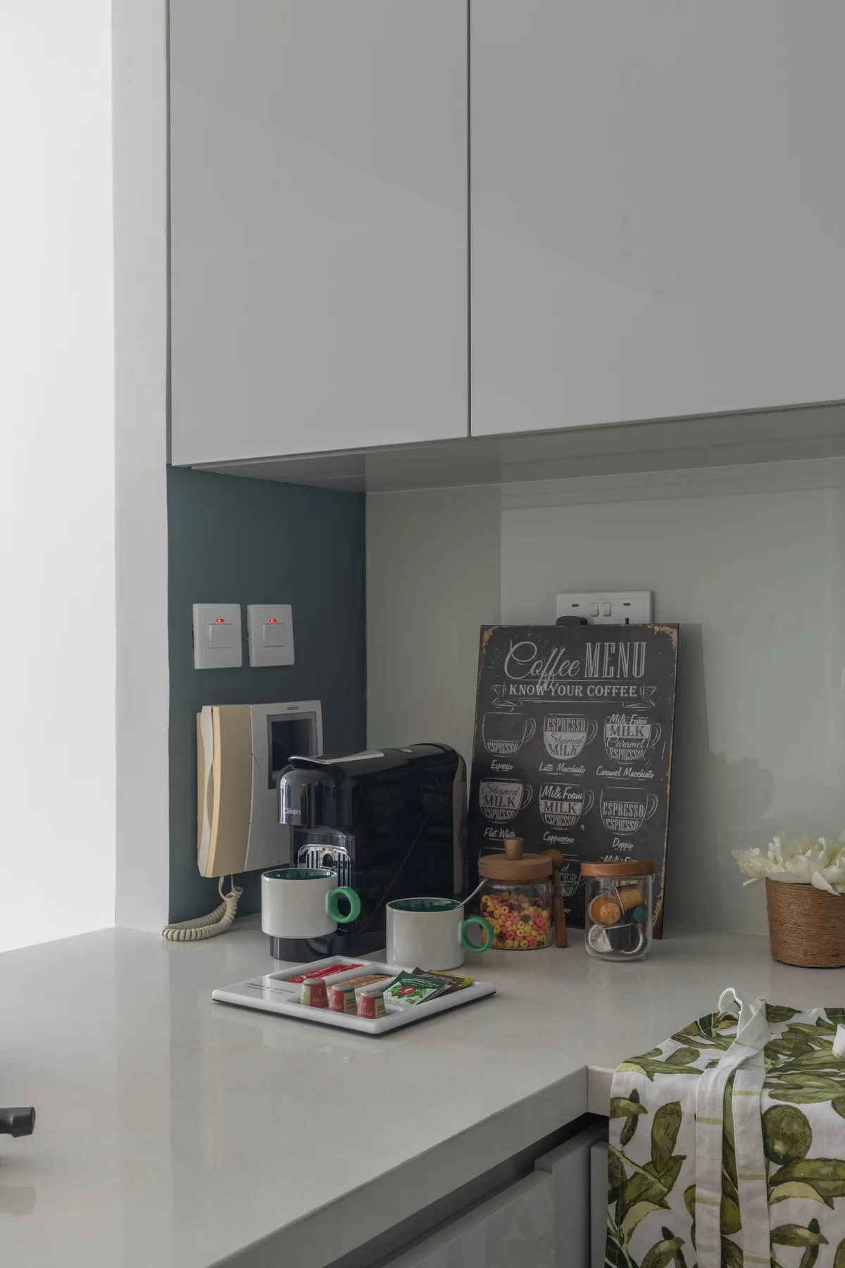 Una encimera de cocina con una cafetera, tazas y un cartel de menú.