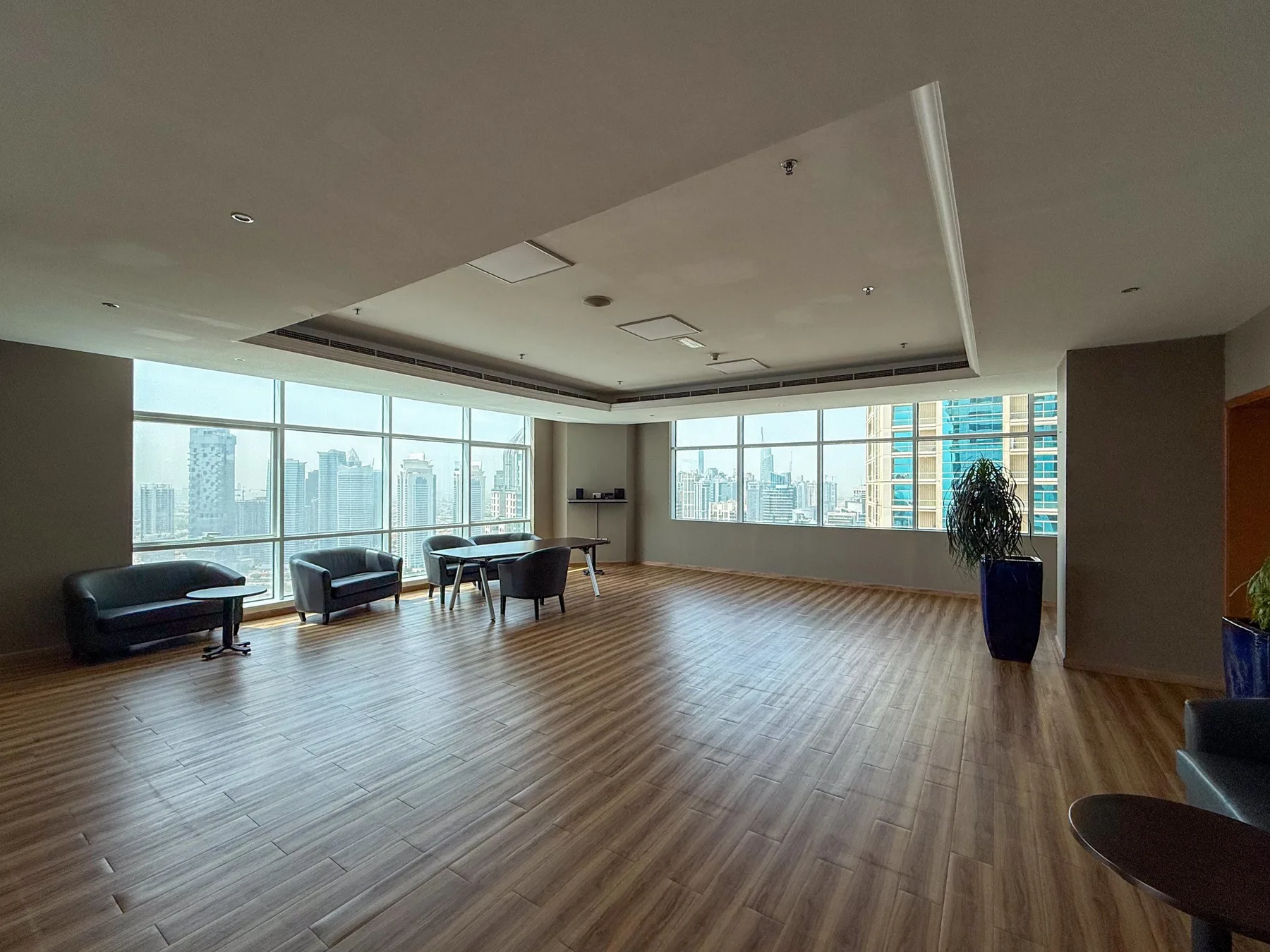 Una amplia sala interior con grandes ventanales, piso de madera y algunas áreas para sentarse.