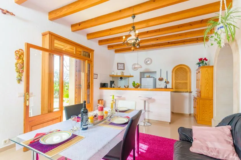 A bright dining and kitchen area with exposed wooden ceiling beams and a table.