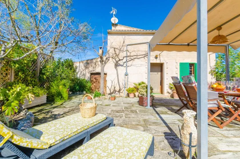 A sunny stone patio with cushioned seating beside a pale house.