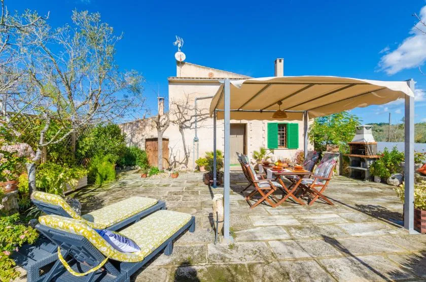 A sunlit stone patio has outdoor seating beneath a fabric canopy.
