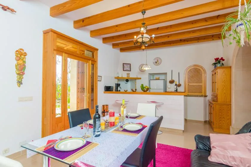 A dining area opens onto a kitchen, with a table set beneath exposed wooden ceiling beams.