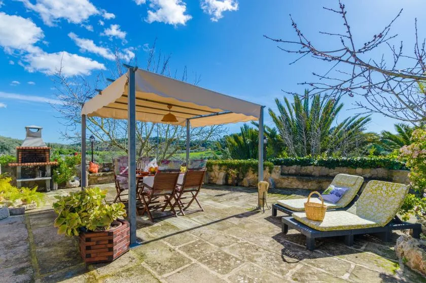 A sunny outdoor terrace has a shaded dining area and cushioned seating.