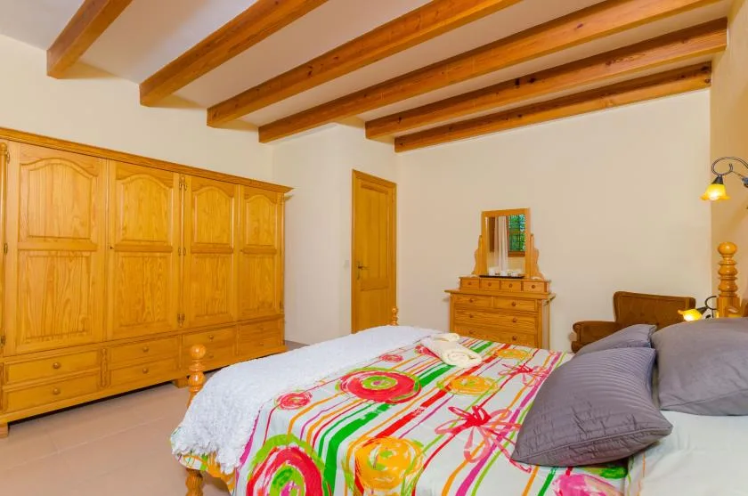 A bedroom with a colorful patterned bedspread and wooden ceiling beams.