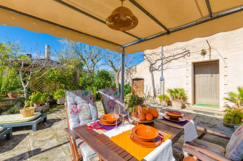 A covered outdoor dining area with a set table and garden surroundings.