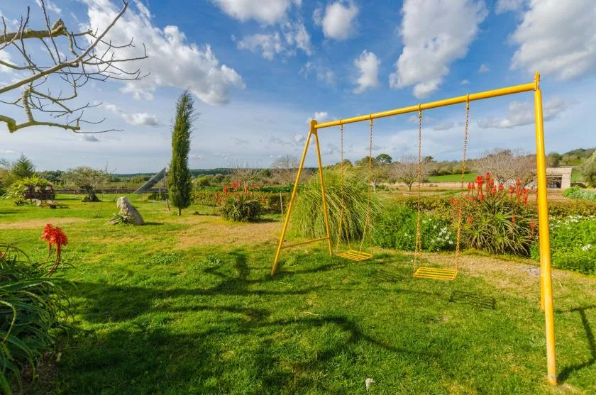 A grassy garden with a yellow swing set and flowering plants.