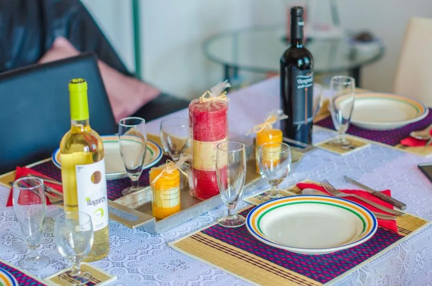 A dining table is set with plates, glasses, candles, and bottles.