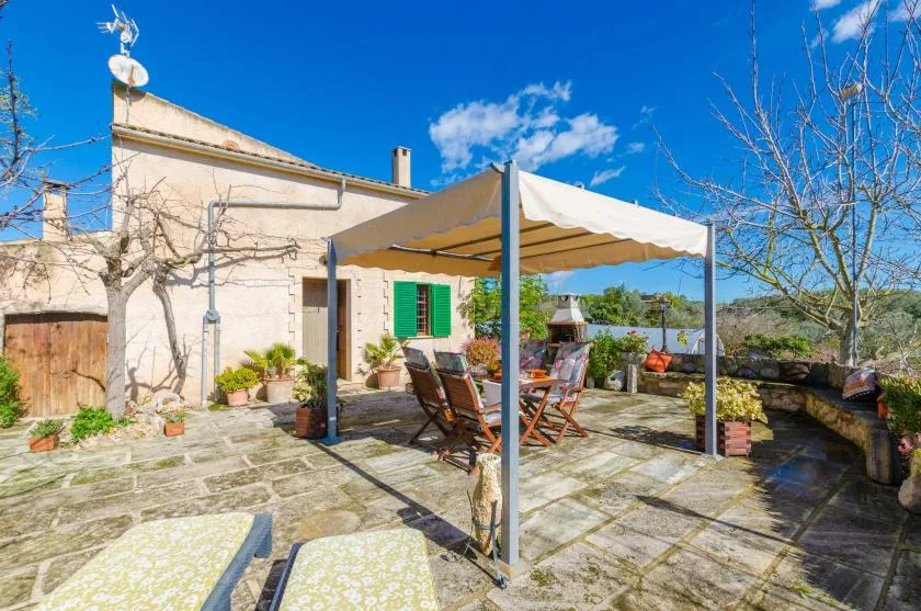 A sunlit stone patio has a shaded seating area beneath a fabric canopy.