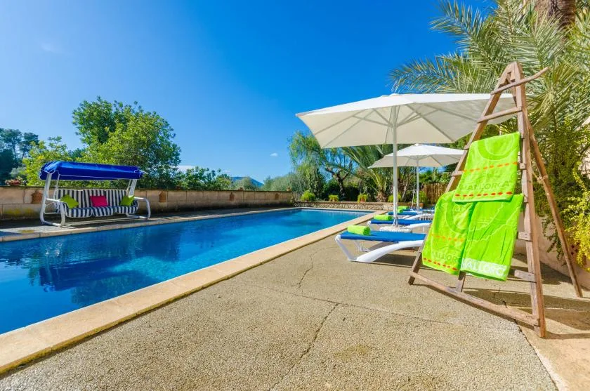 An outdoor swimming pool is lined with sun loungers and large shade umbrellas.