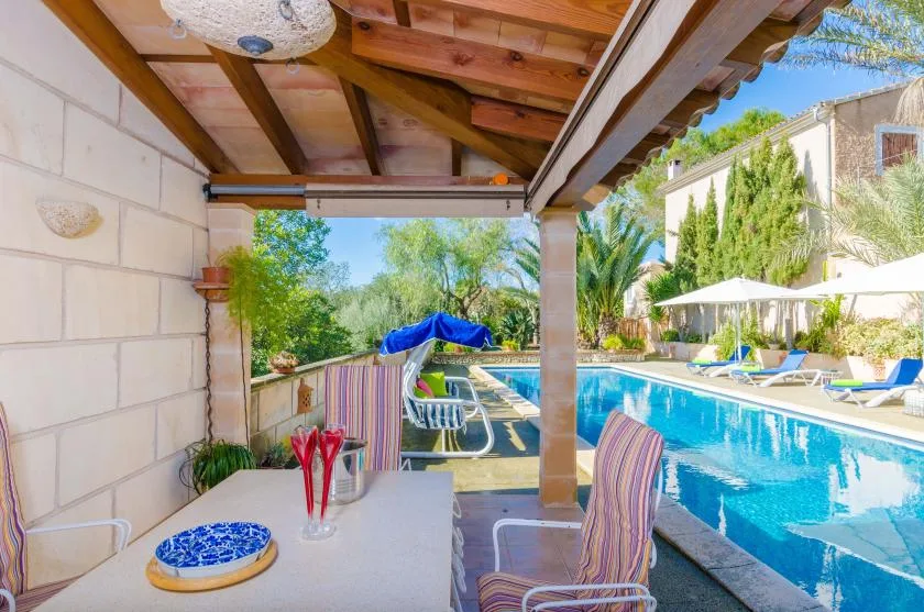 Covered poolside patio with a table and seating beside a swimming pool.