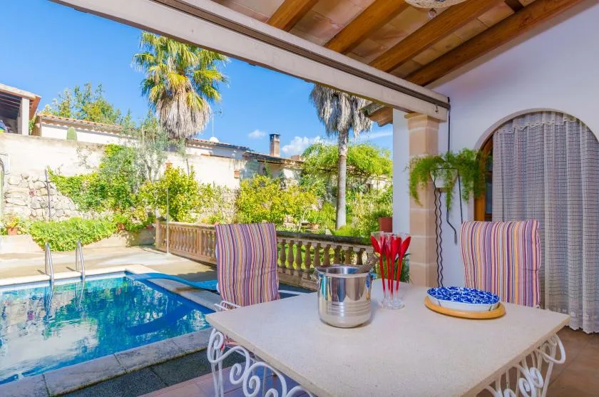 A covered patio dining area overlooks a swimming pool and leafy garden.