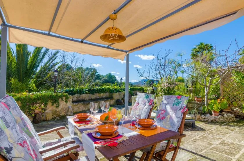 An outdoor dining area sits beneath a canopy, with a table set for a meal.