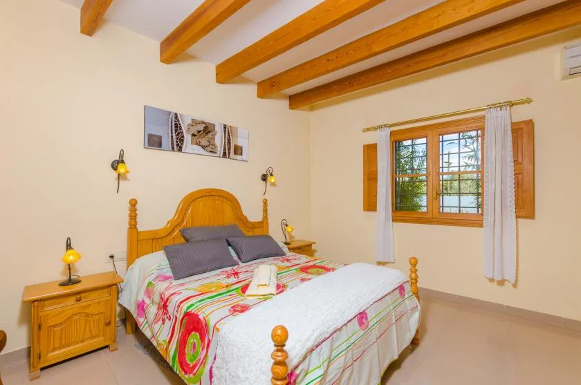 A bedroom with a wooden bed, colorful bedding, and a window.