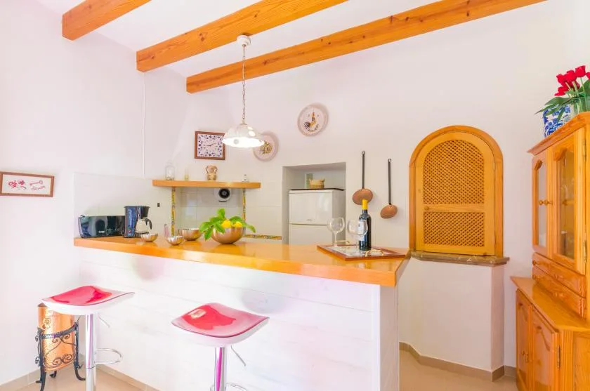 A bright kitchen with a white counter, wooden bar top, and overhead beams.