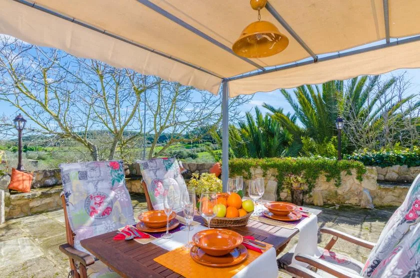 A shaded outdoor dining area with a table set with dishes and fruit.