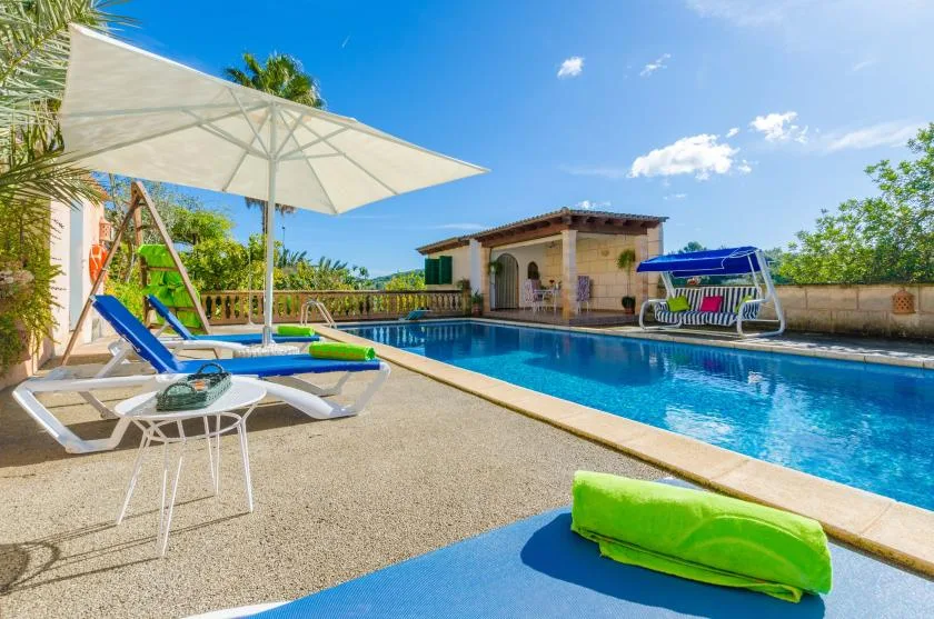 An outdoor swimming pool beside a paved patio with loungers and an umbrella.