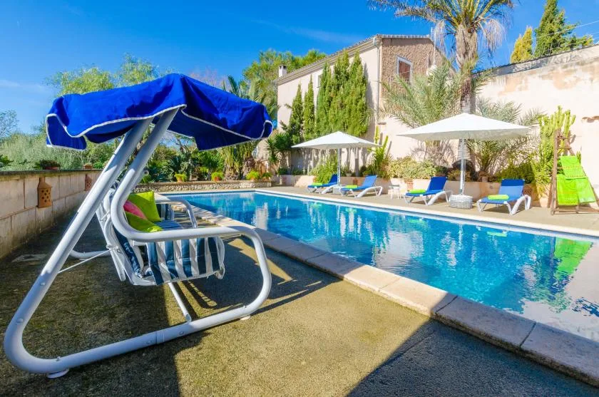 An outdoor swimming pool with lounge seating and umbrellas beside a building.