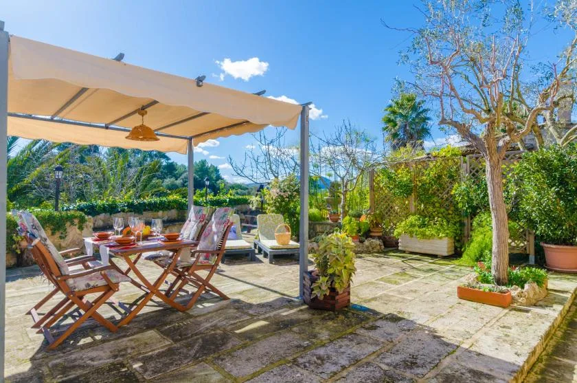An outdoor dining terrace sits beneath a canopy, surrounded by potted plants and trees.