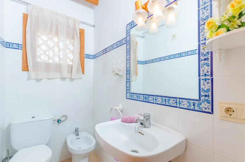 A bright tiled bathroom with a sink, mirror, and curtained window.