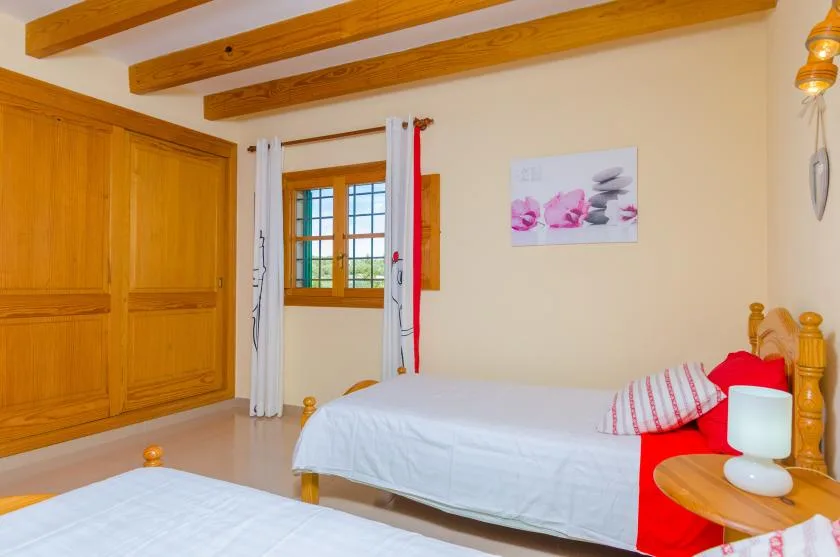 A bedroom with beds, a wooden wardrobe, and a curtained window.