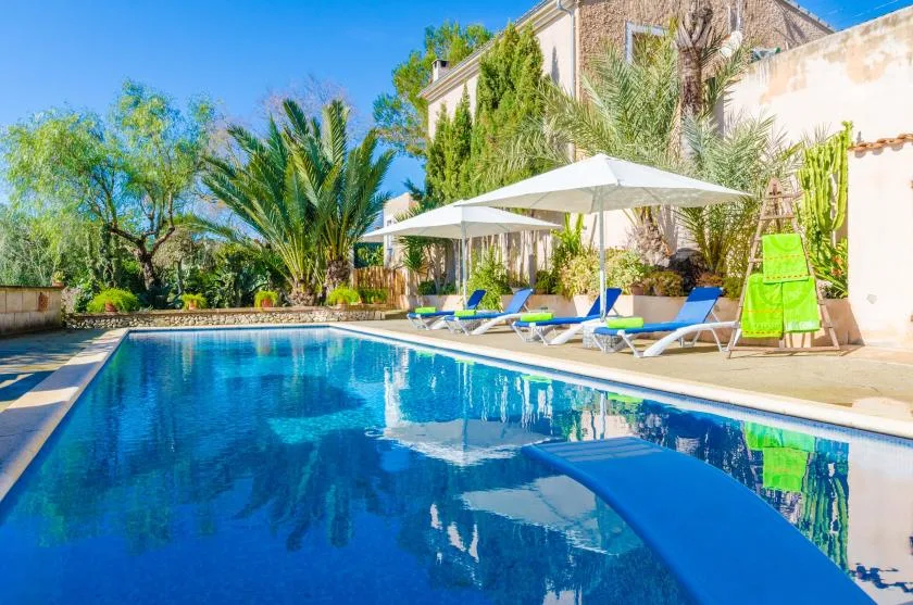 Outdoor swimming pool with lounge seating, parasols, and surrounding greenery.