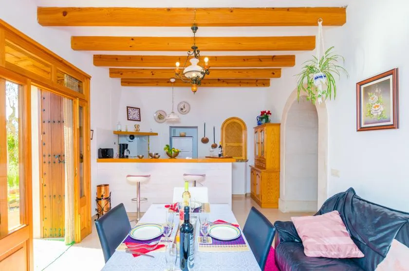 A bright dining area opens onto a kitchen, with a table beneath exposed wooden ceiling beams.