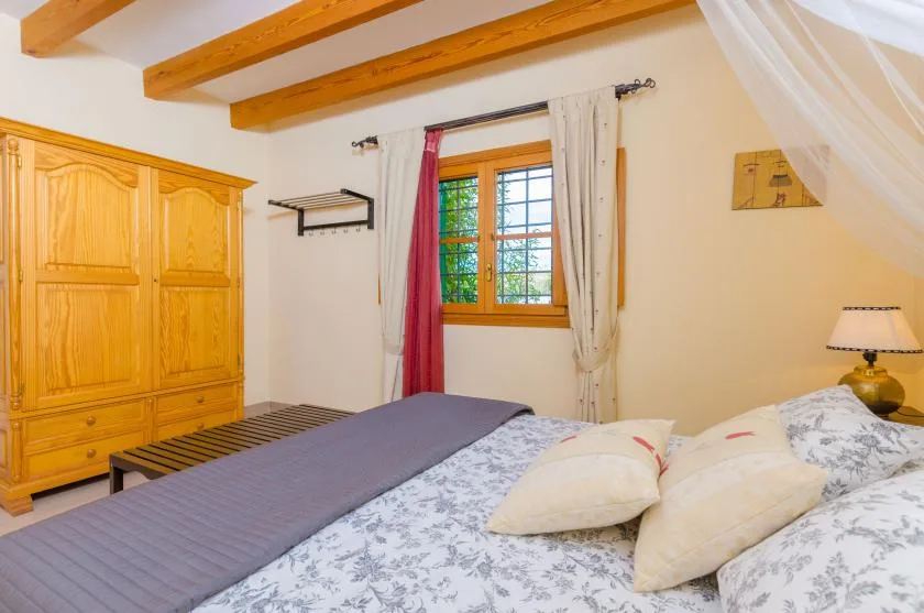 A bedroom with a large bed, wooden wardrobe, and window.