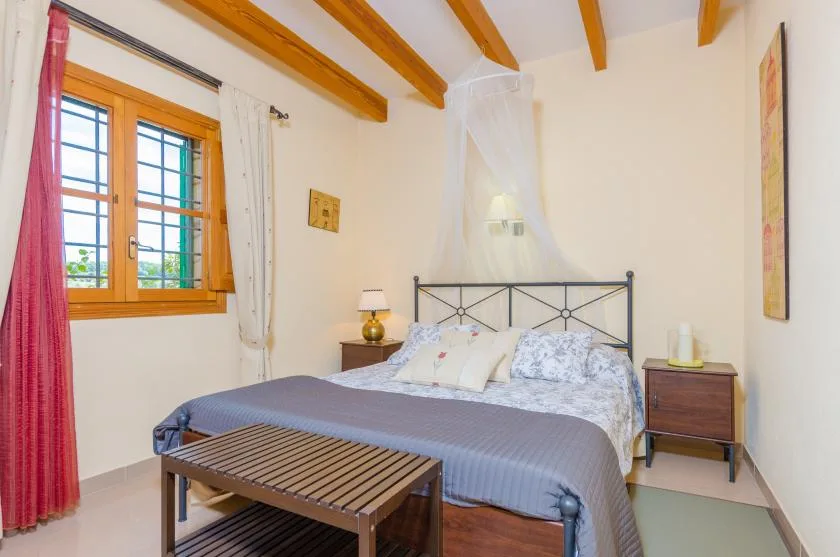 A bedroom with a bed beneath exposed wooden ceiling beams.