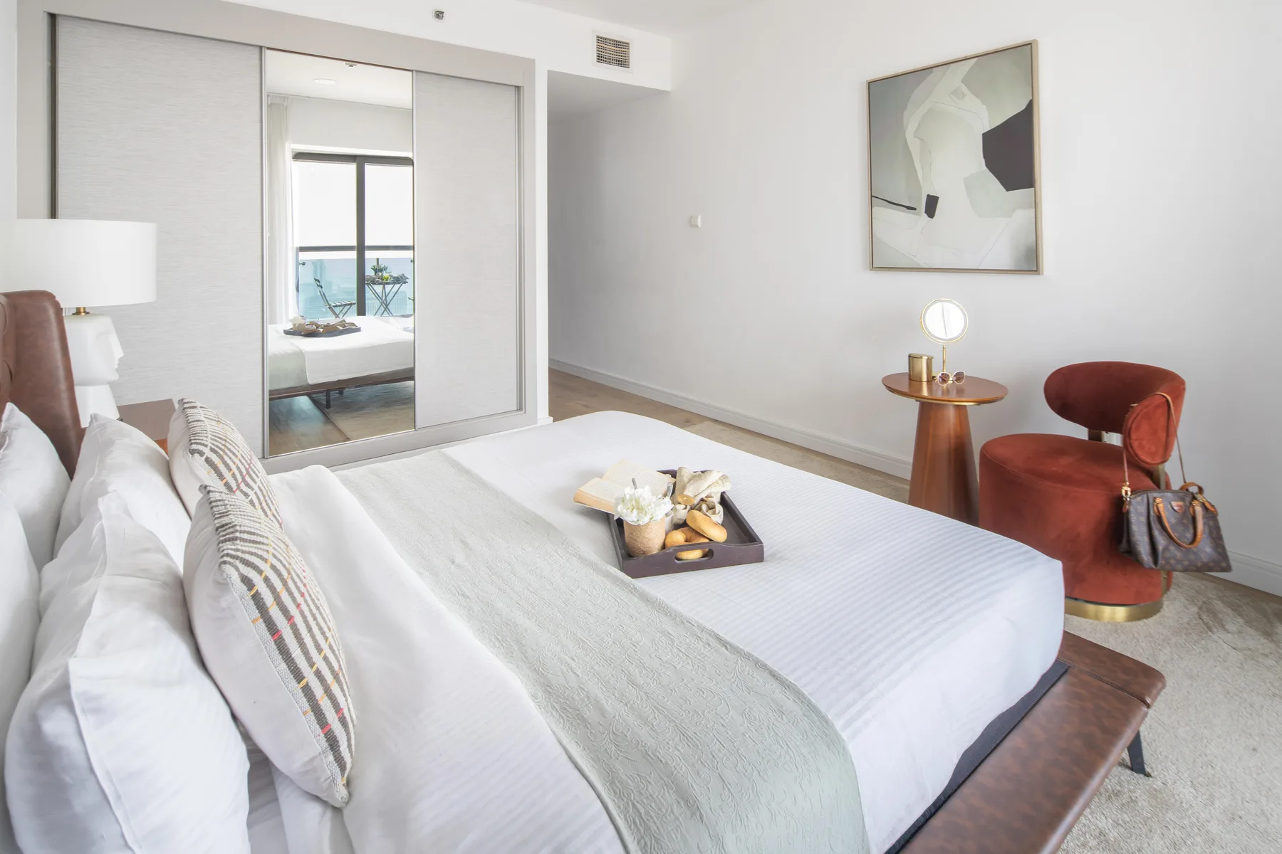 Un dormitorio luminoso con una cama bien tendida y un sillón rojo.