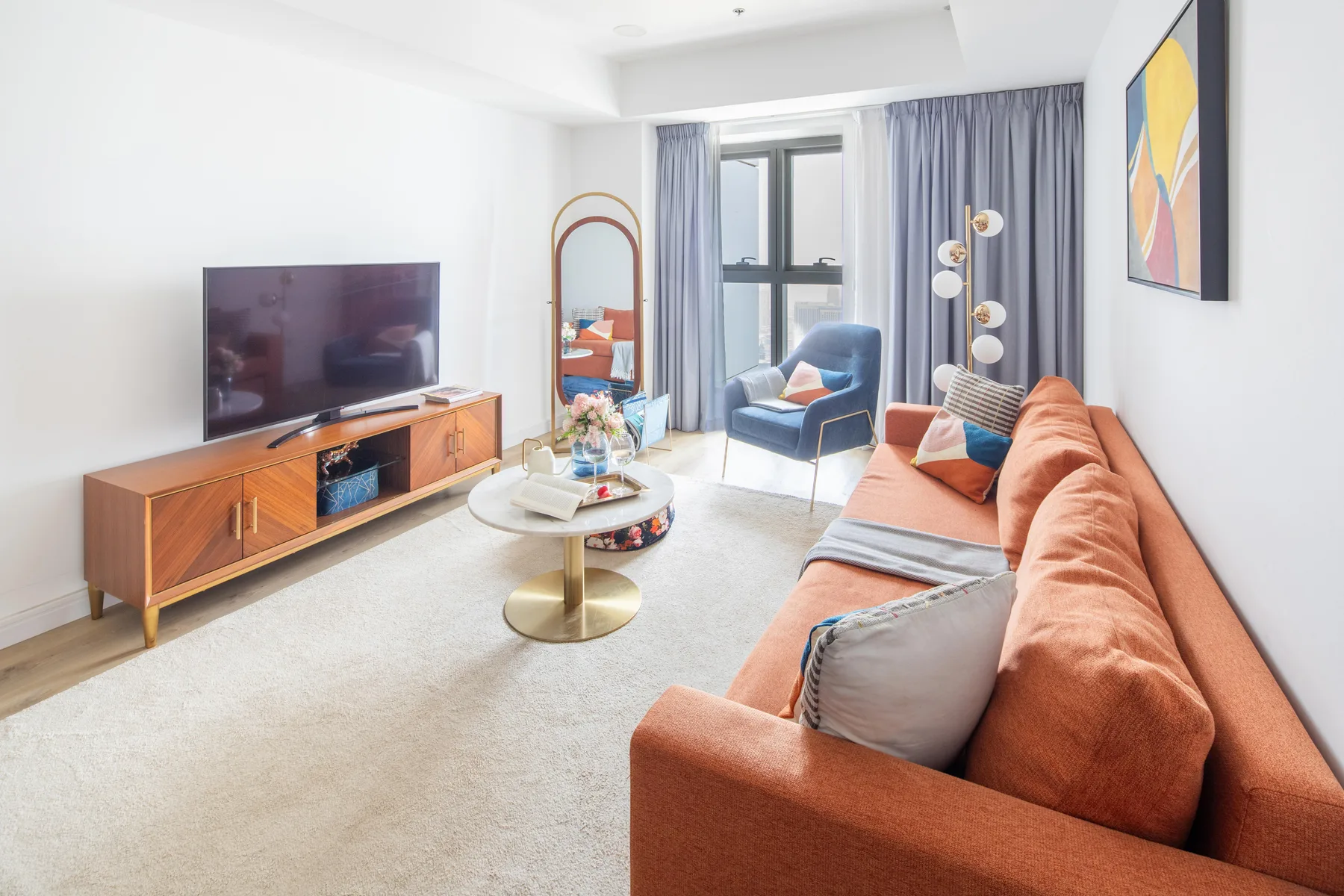 Una sala luminosa con un sofá color óxido y un televisor sobre un mueble de madera.