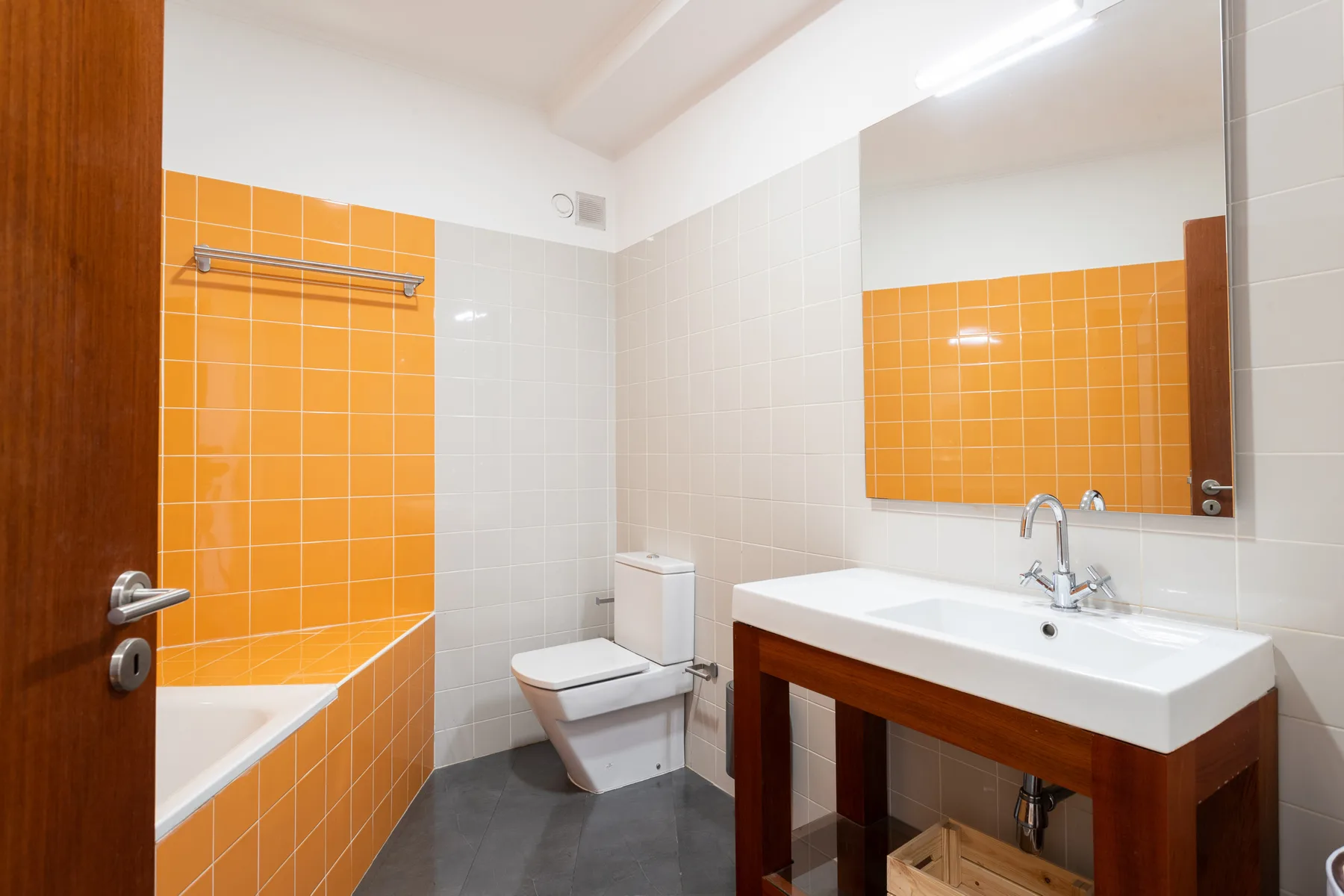 A tiled bathroom with a bathtub, toilet, and sink beneath a large mirror.