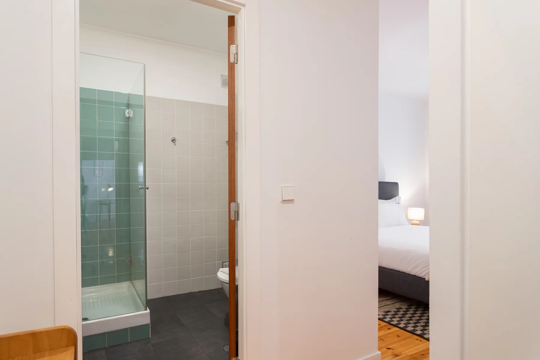 A bathroom with a glass shower beside a doorway to a bedroom.