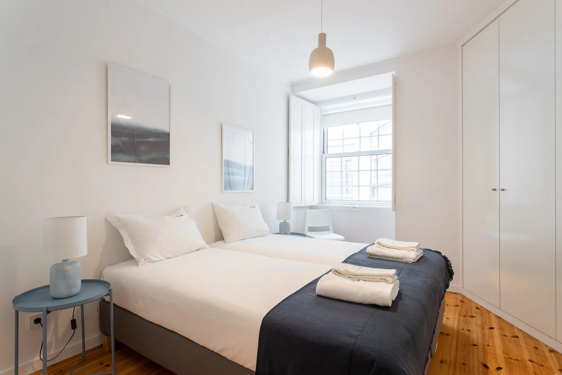 A bright bedroom with a neatly made bed beside a window.