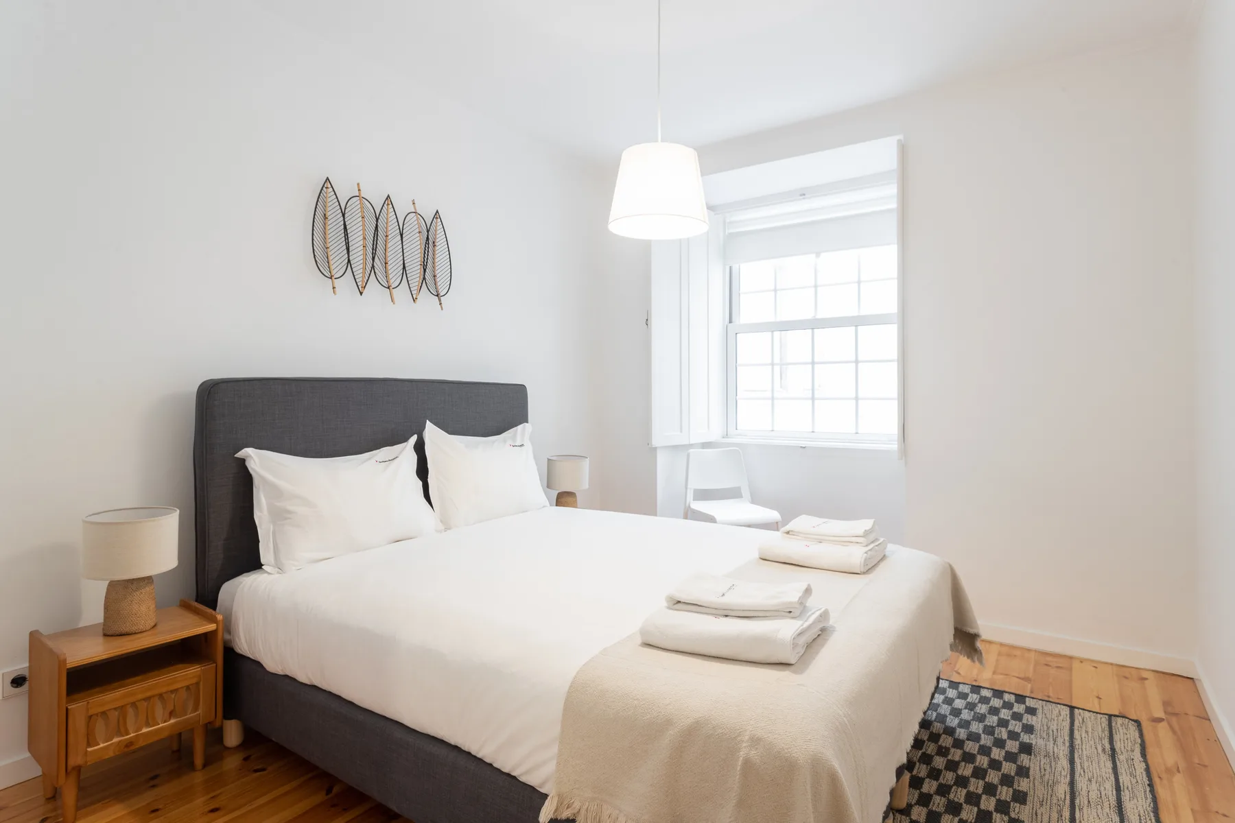 A bright bedroom with a bed, bedside table, and window.