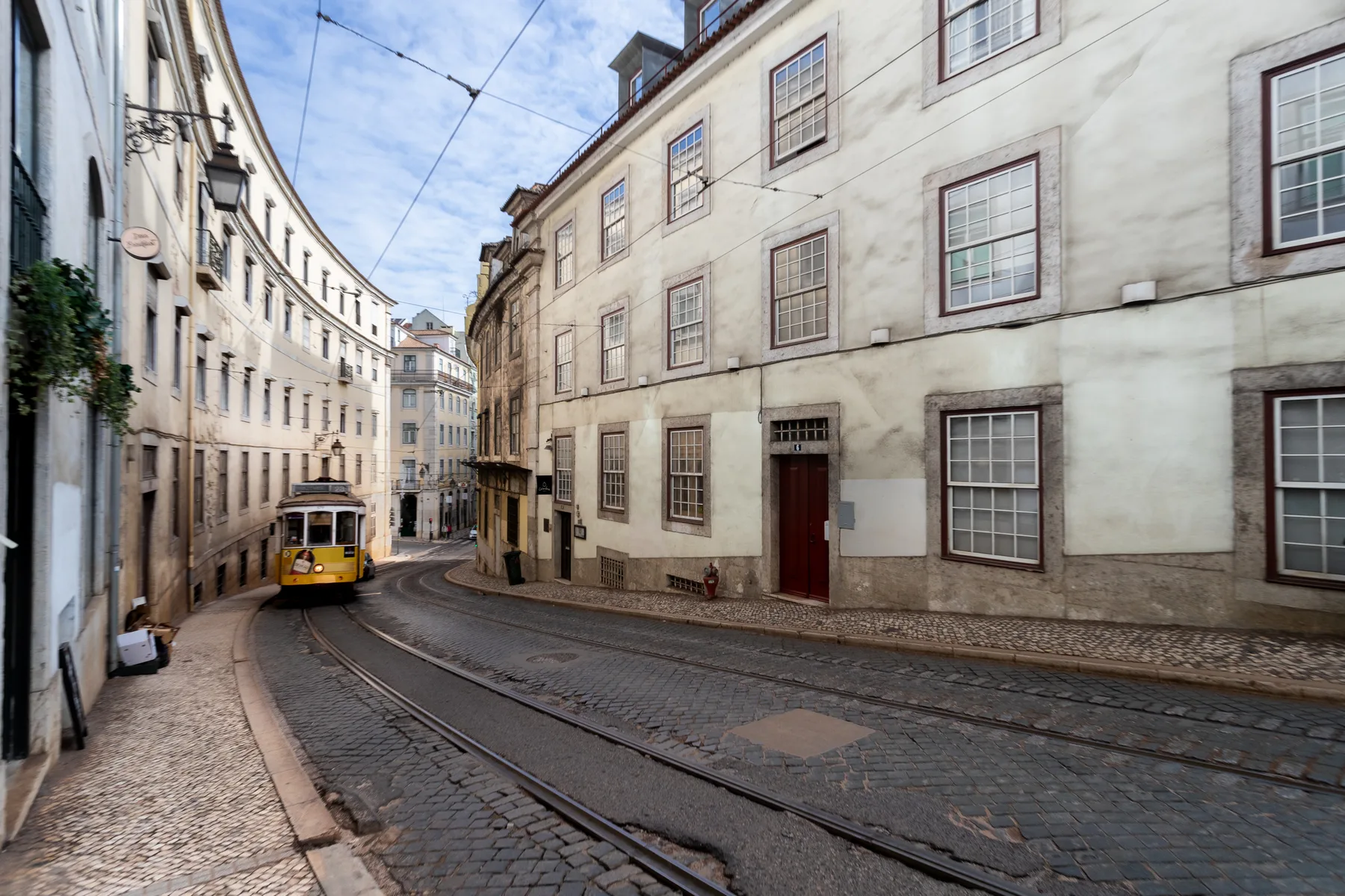 A narrow cobblestone street curves between old buildings, with a yellow tram.