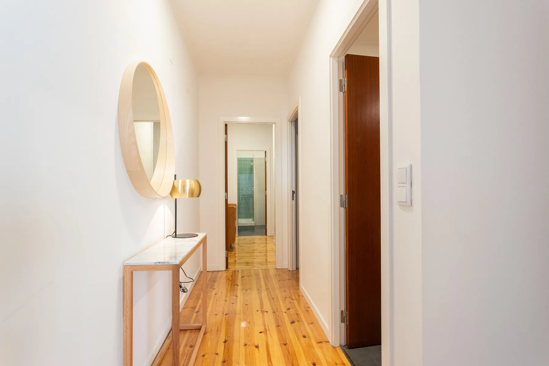 A bright hallway with wooden flooring and a console table beneath a round mirror.