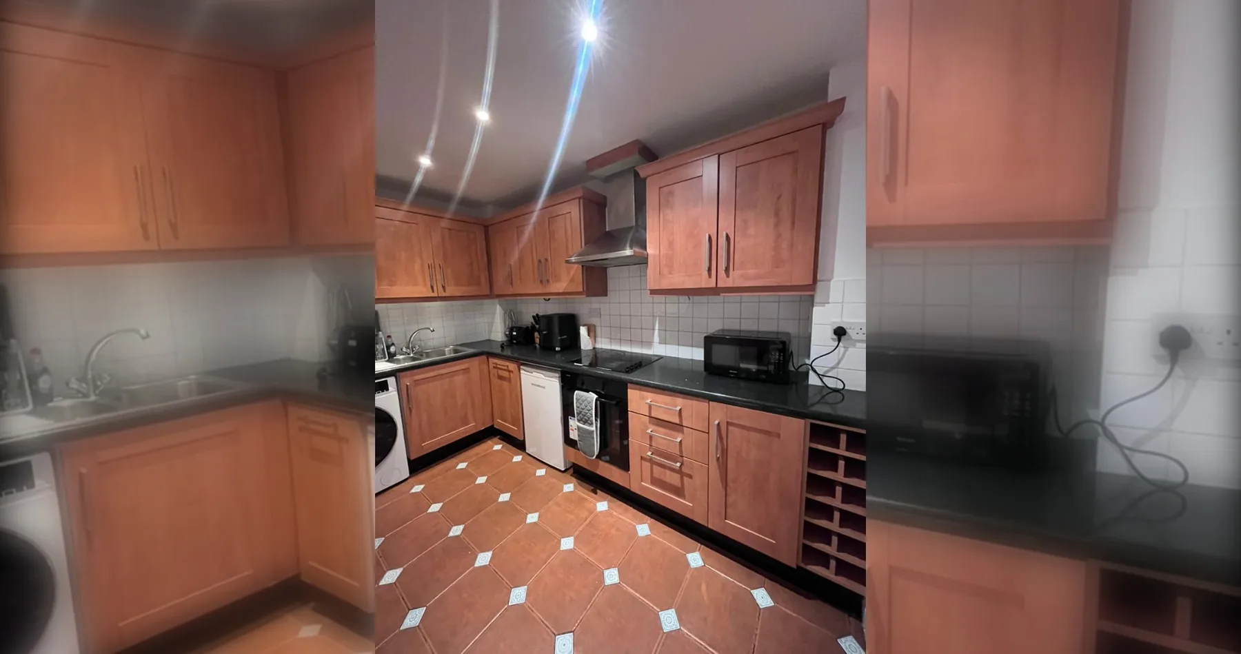 Una cocina con armarios de madera, encimeras oscuras y suelo de baldosas.
