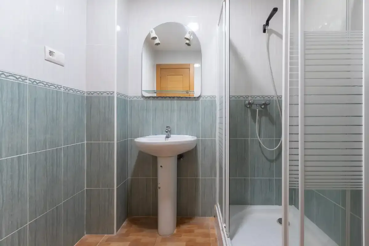 Un baño alicatado con lavabo de pedestal, espejo y ducha.
