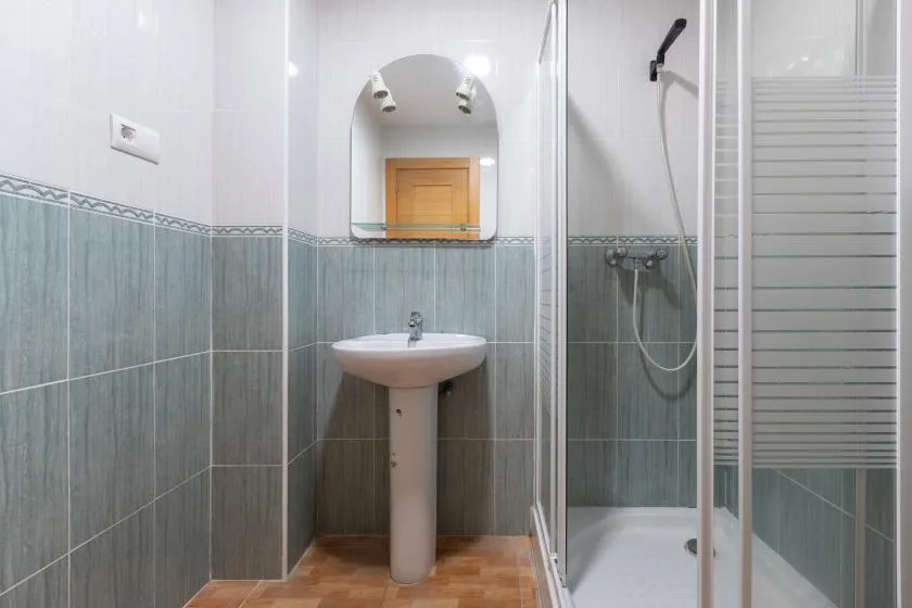 Un baño alicatado con lavabo de pedestal, espejo y ducha de cristal.