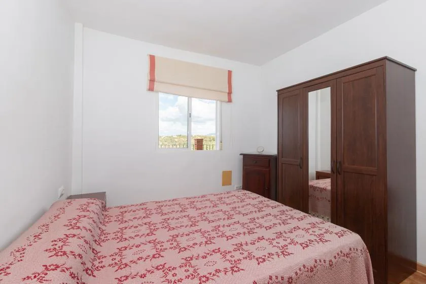 Un dormitorio con una colcha estampada, una ventana y un armario de madera oscura.