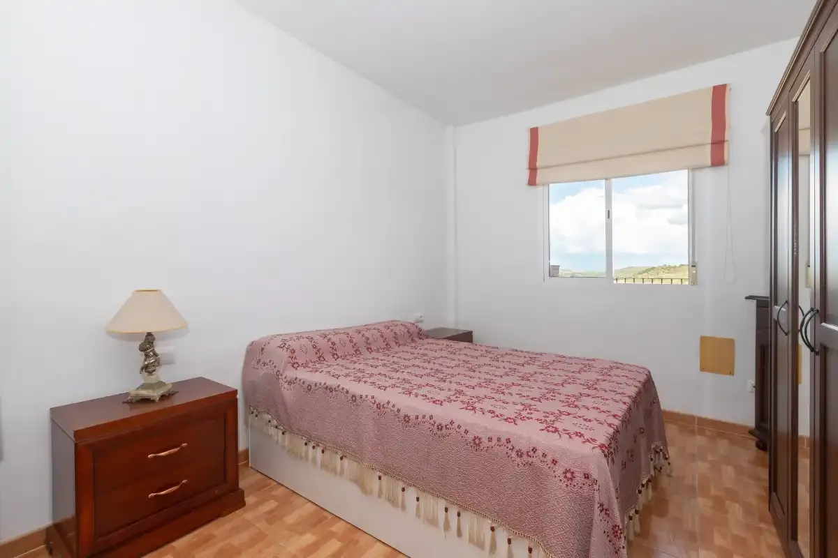 Un dormitorio con una cama doble, una mesita y una ventana.