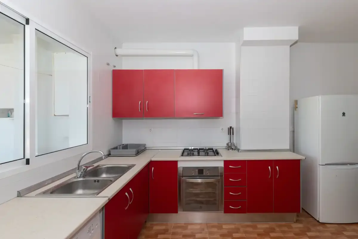 Una cocina luminosa con armarios rojos, un fregadero y una estufa.