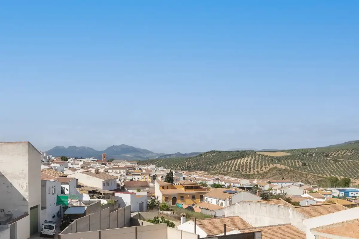 Un pueblo se extiende en primer plano bajo colinas bajas y un cielo azul despejado.